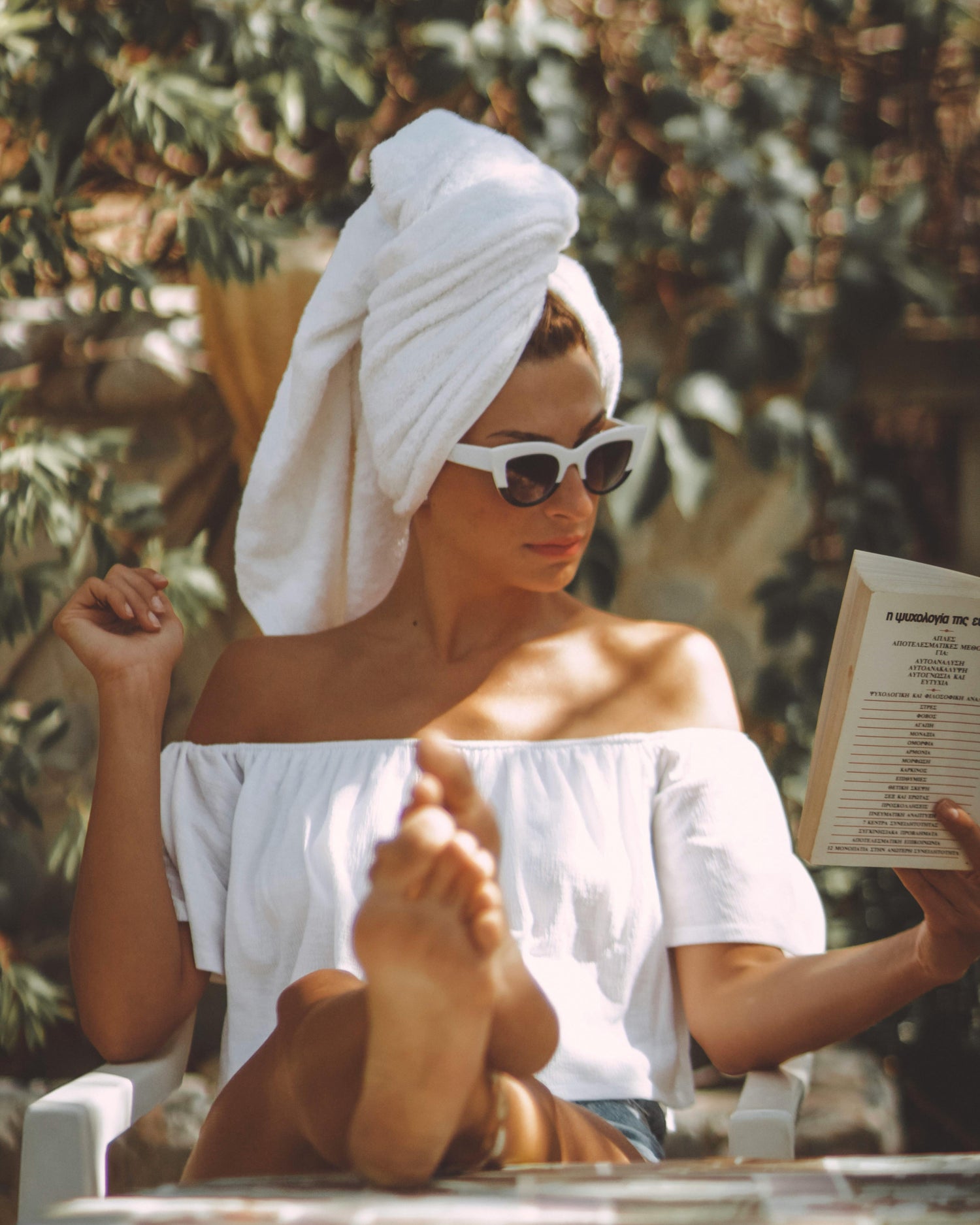 Woman with a towel wrapped around her head, reading a book outdoors.